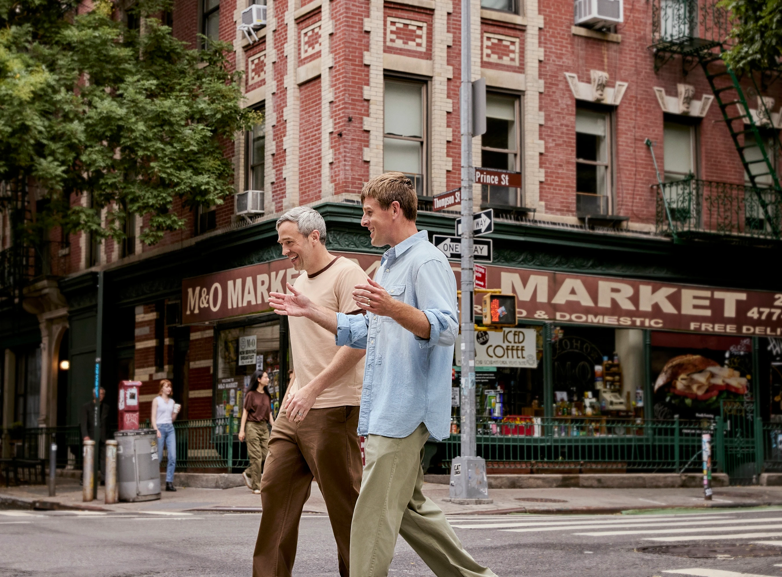 Two men laughing as they cross a New York street outside a corner market