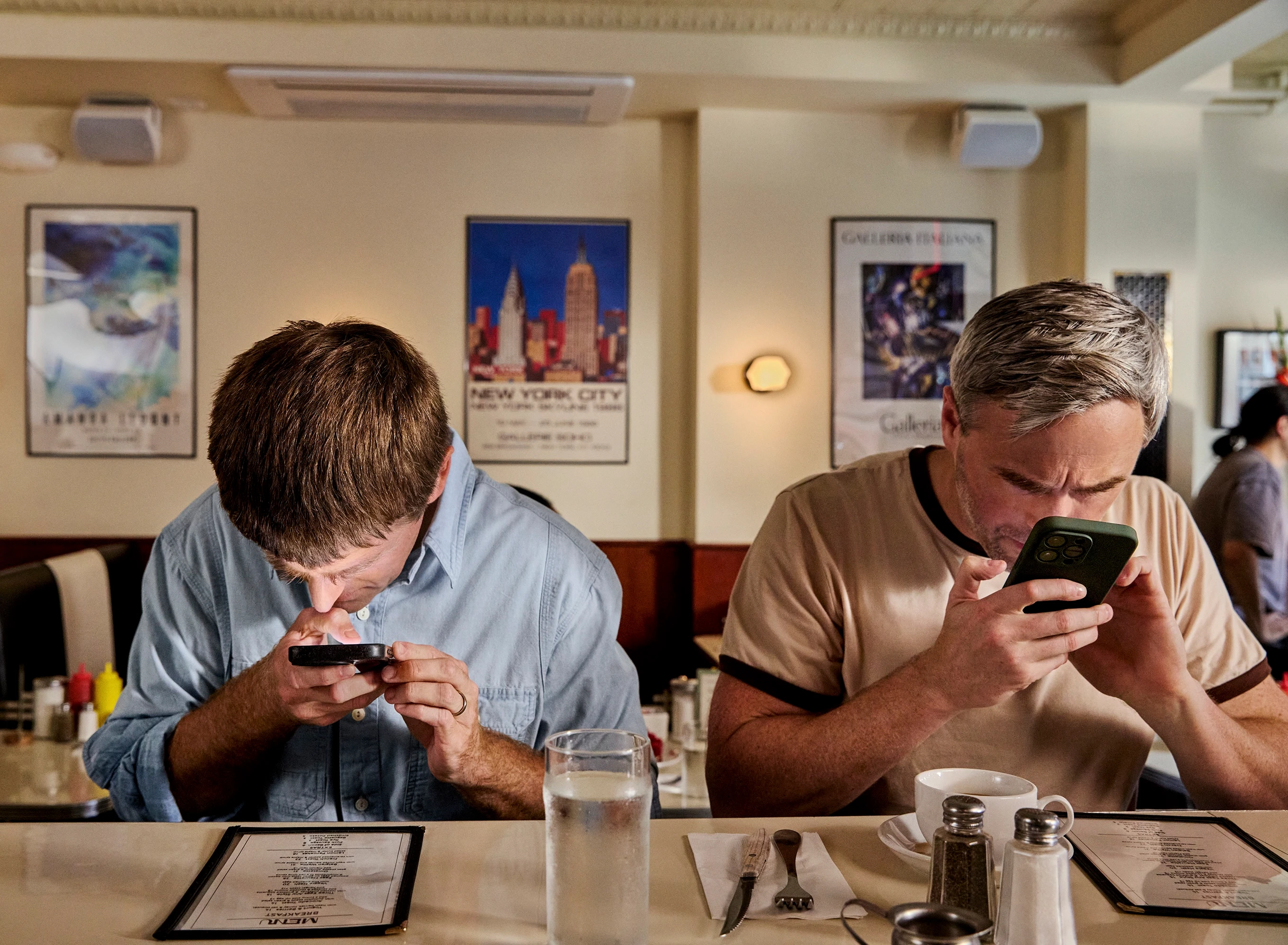 Two men at a diner counter, both bent over their phones