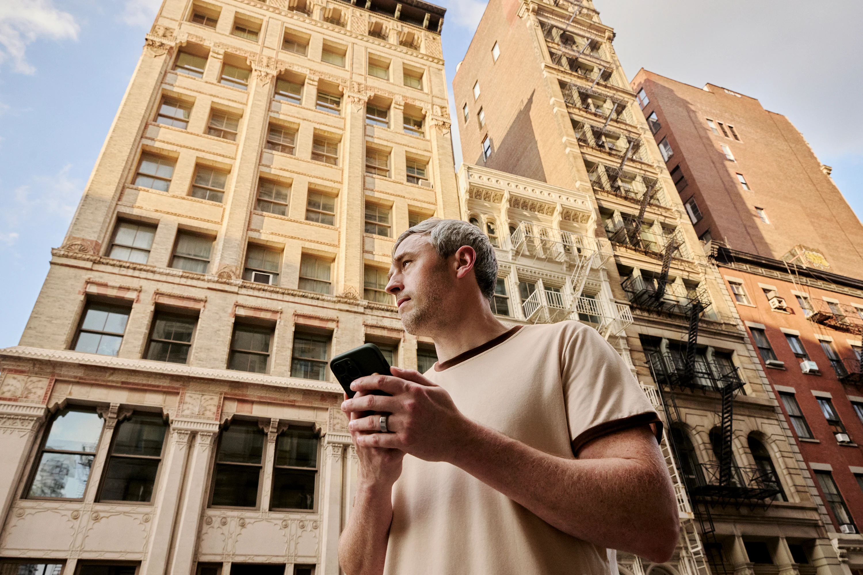 A man with his phone in hand, looking up the street between tall buildings